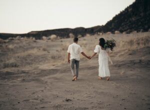 unrecognizable wedding barefoot couple walking on sandy terrain
