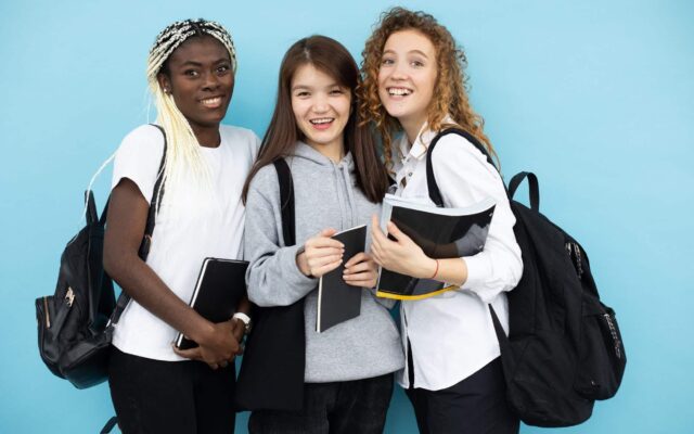 joyful diverse female students standing with books in studio