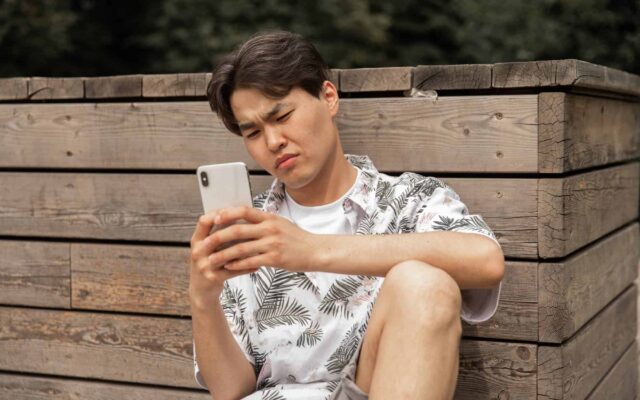 asian displeased man browsing smartphone in countryside