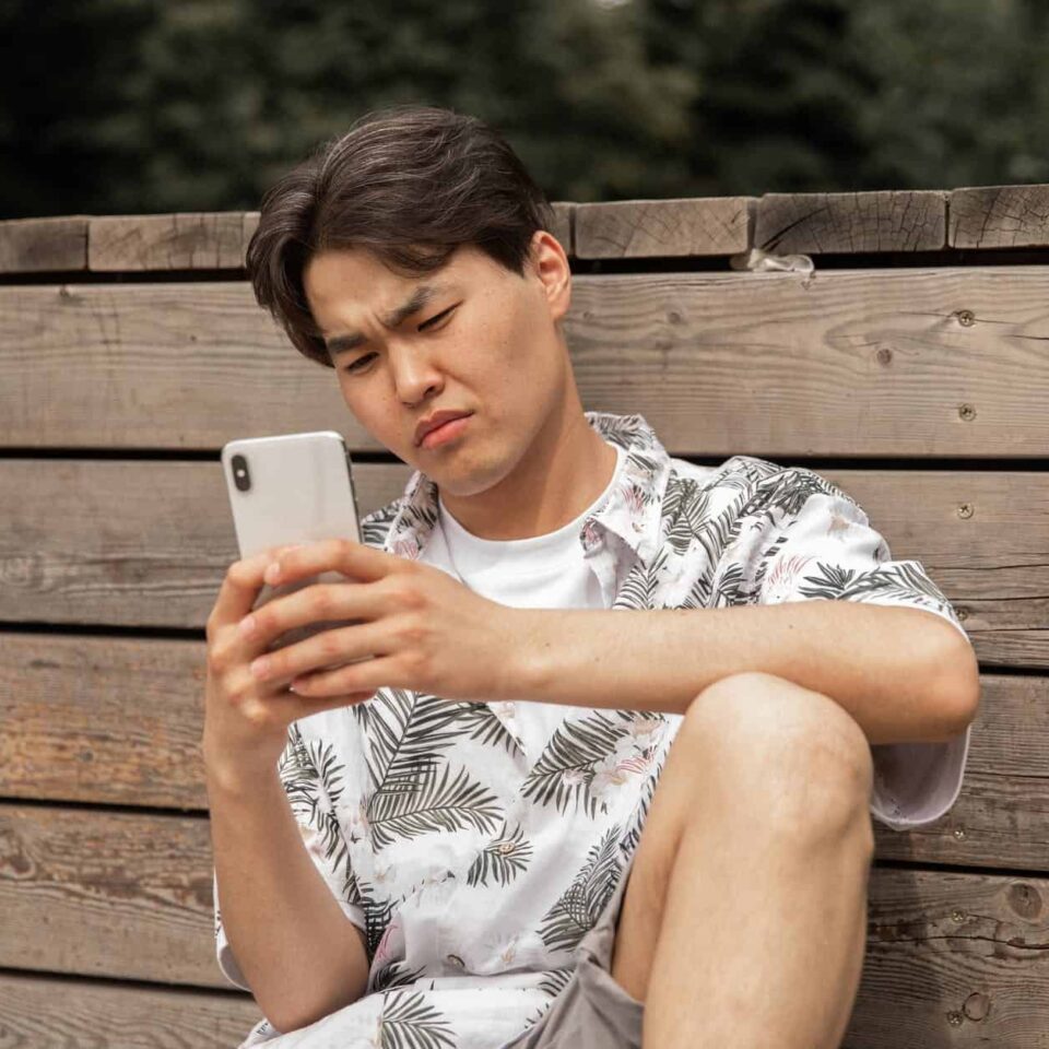 asian displeased man browsing smartphone in countryside
