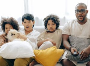 interested multiracial family watching tv on sofa together with dog