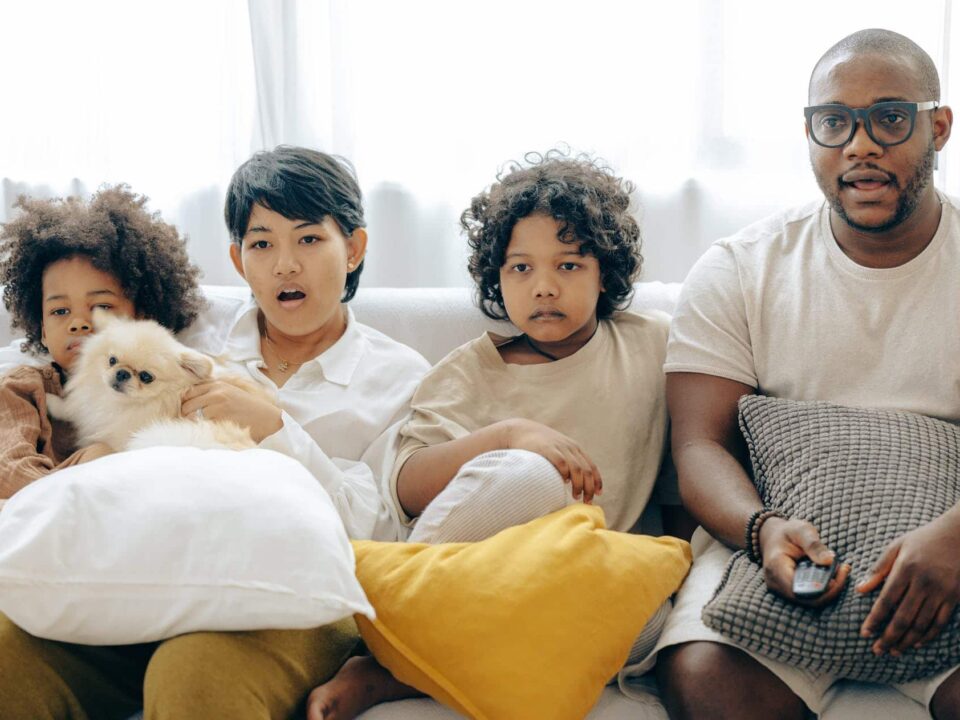 interested multiracial family watching tv on sofa together with dog