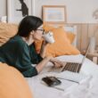 woman using laptop and drinking beverage in bed